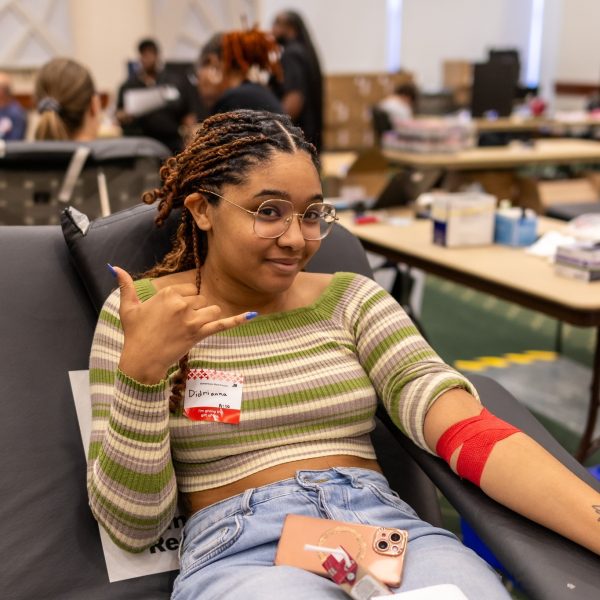 UNC Charlotte student laying on a medical table to give blood smiles and gives the "picks up" hand gesture