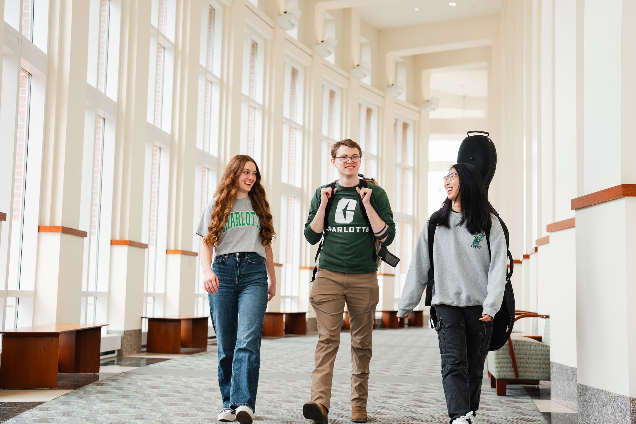 three students walking with their instruments in Robinson Hall, laughing and talking